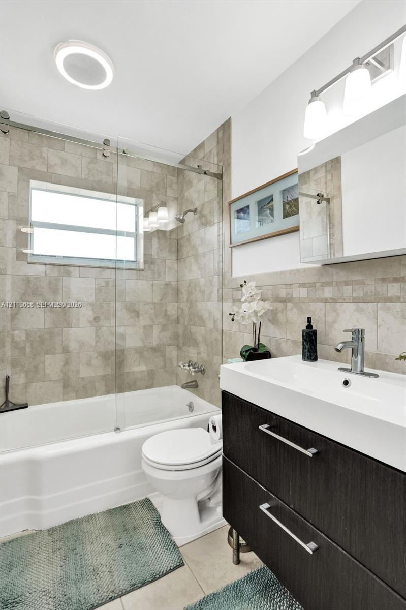 Bathroom featuring a modern floating vanity with a rectangular sink, a glass-panel tub enclosure, floor-to-ceiling tile surrounds, and polished chrome fixtures