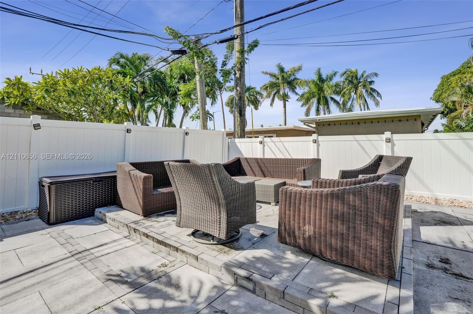 Raised stone paver patio featuring a concrete block border and white privacy fencing