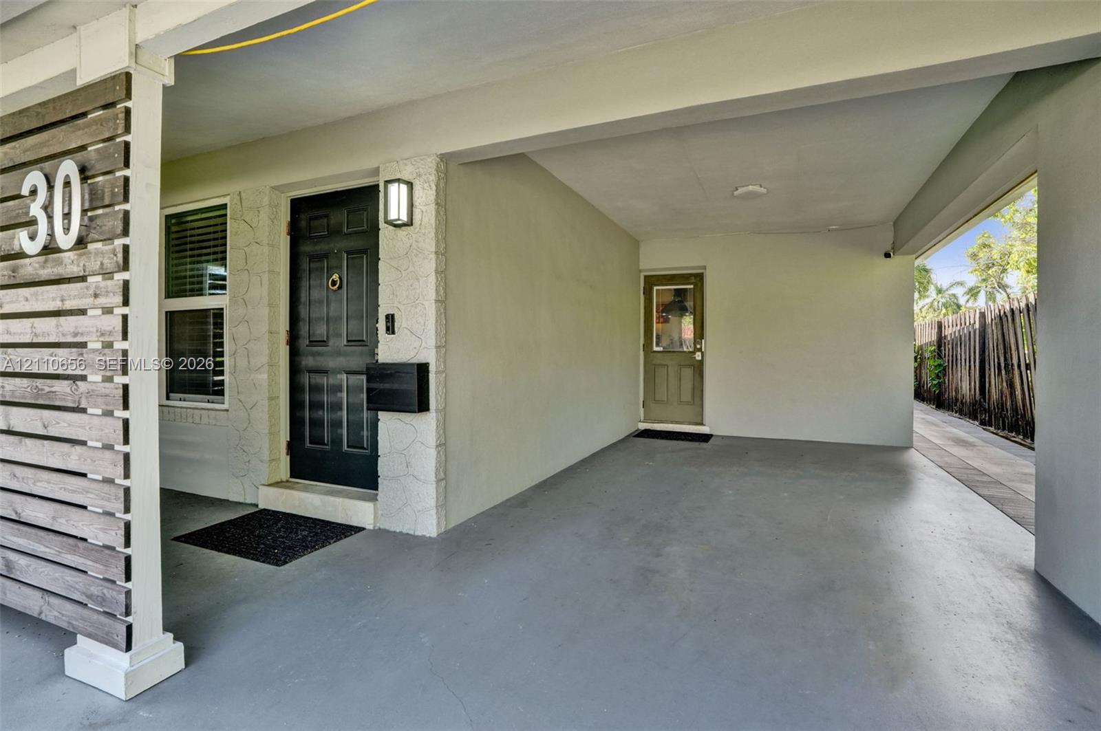 Covered carport featuring horizontal wood-slat privacy screening, a dark-toned entry door with a knocker, exterior stone-veneer accents, and a secondary side-access door