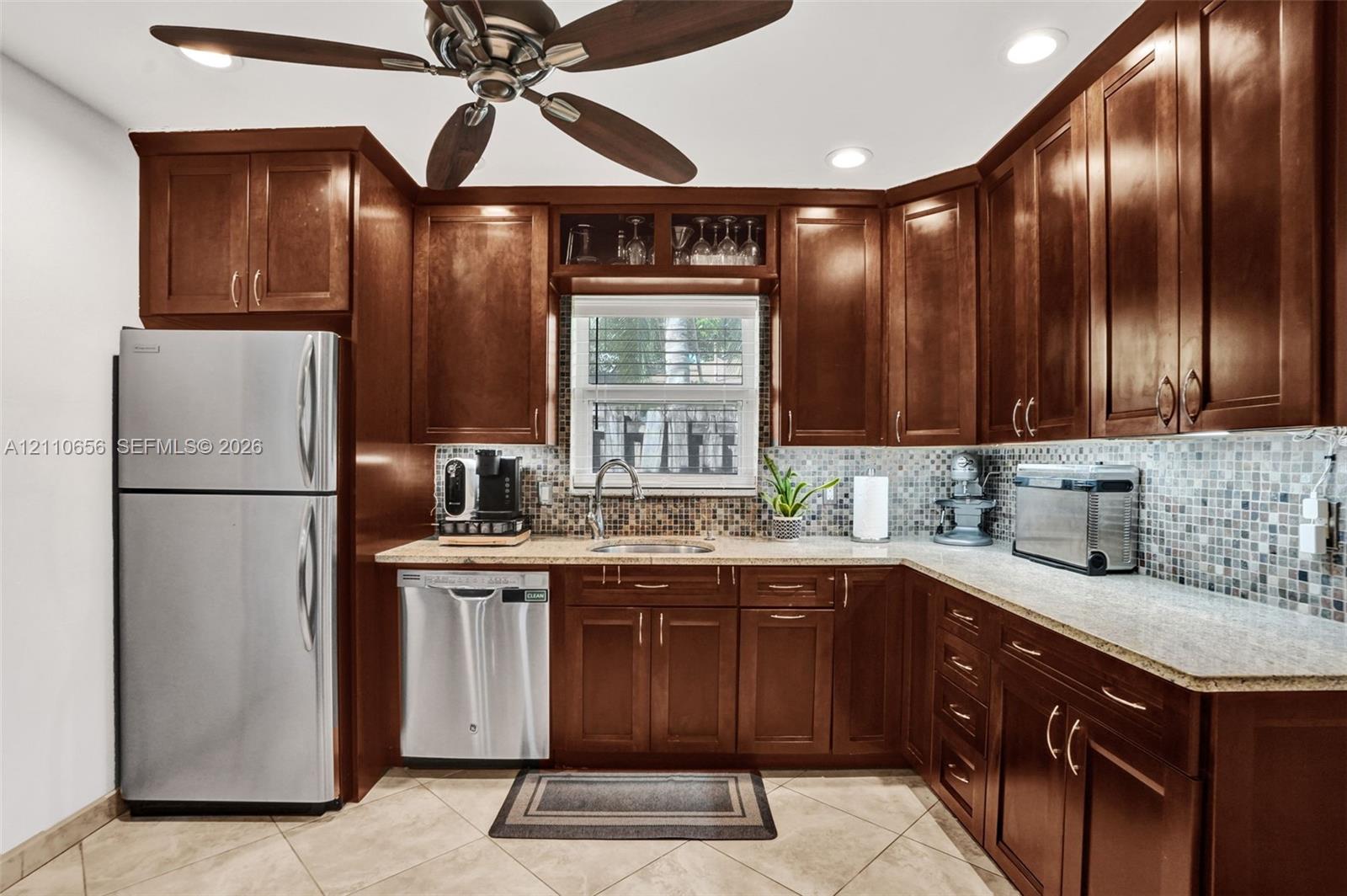 Kitchen featuring stained-wood cabinetry, stone-finish countertops, mosaic tile backsplash, stainless steel appliances, and tile flooring