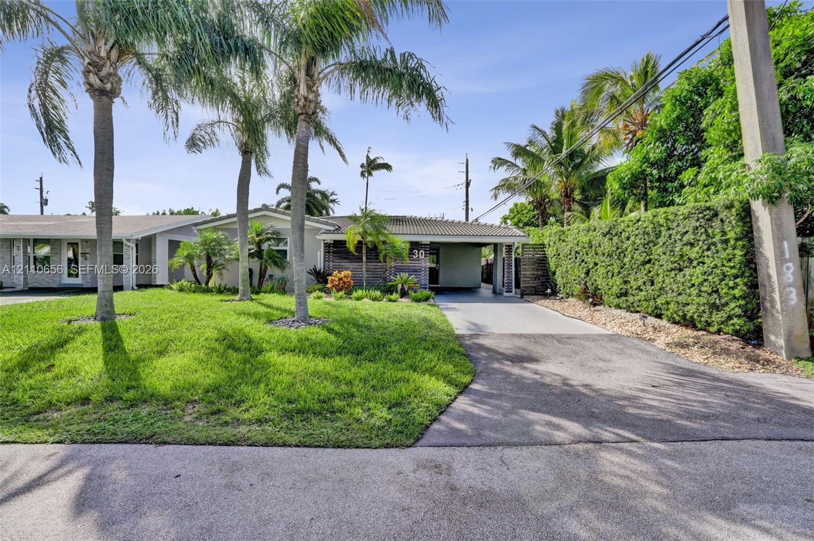 Exterior featuring a concrete tile roof, paved driveway with an integrated carport, established palm trees, and manicured landscaping