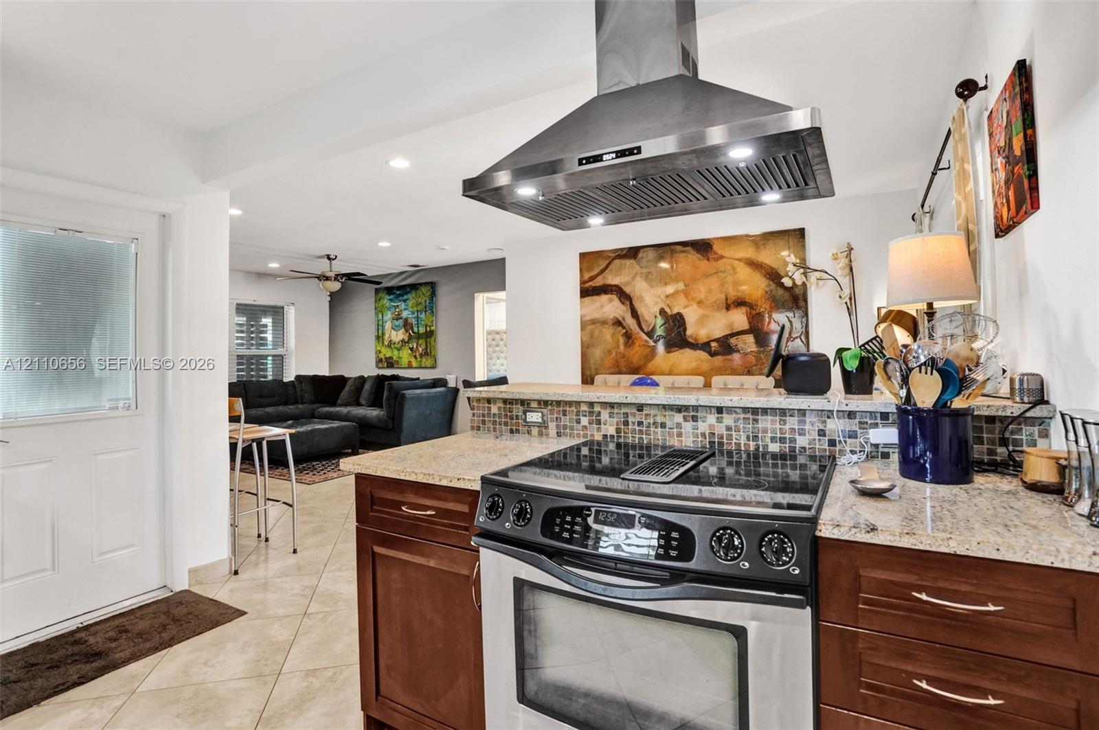 Kitchen featuring dark-finish cabinetry, stone-style countertops, mosaic tile backsplash, and a stainless steel range hood