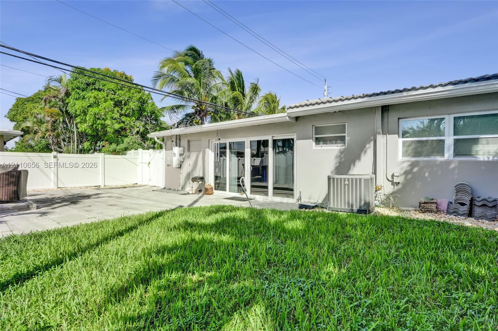 Rear exterior featuring a concrete patio, sliding glass doors, a white vinyl privacy fence, and mature palm trees