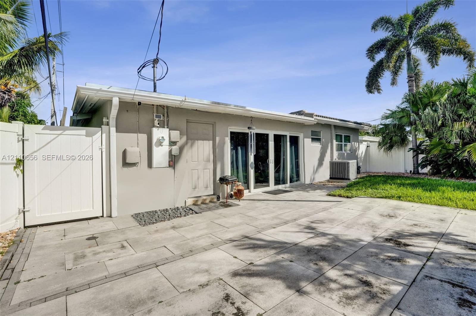 Rear exterior featuring a concrete paver patio, sliding glass doors, a solid-panel white privacy gate, and manicured lawn space