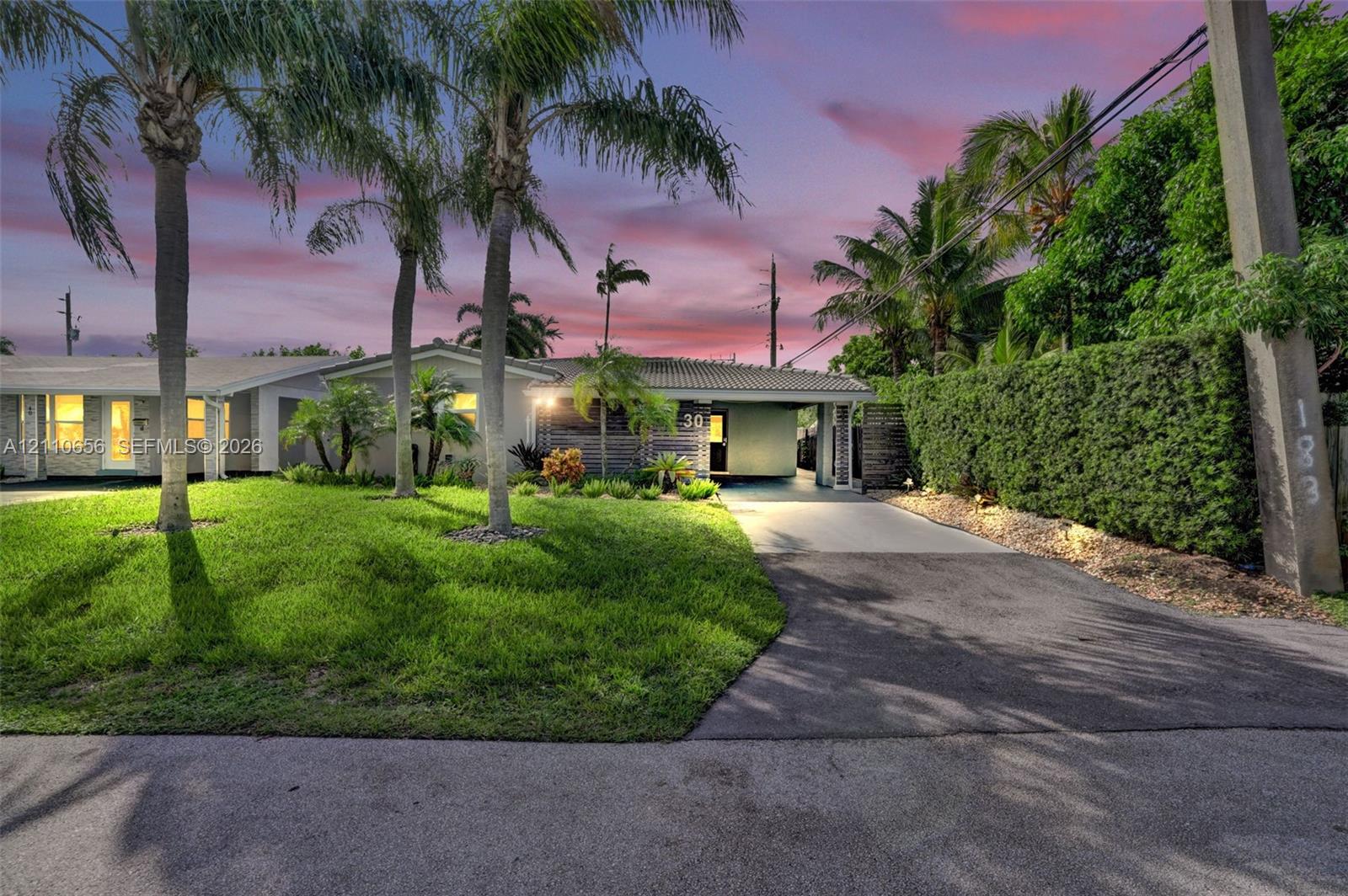 Single-story exterior featuring a concrete tile roof, attached covered carport, paved driveway, and mature landscaping