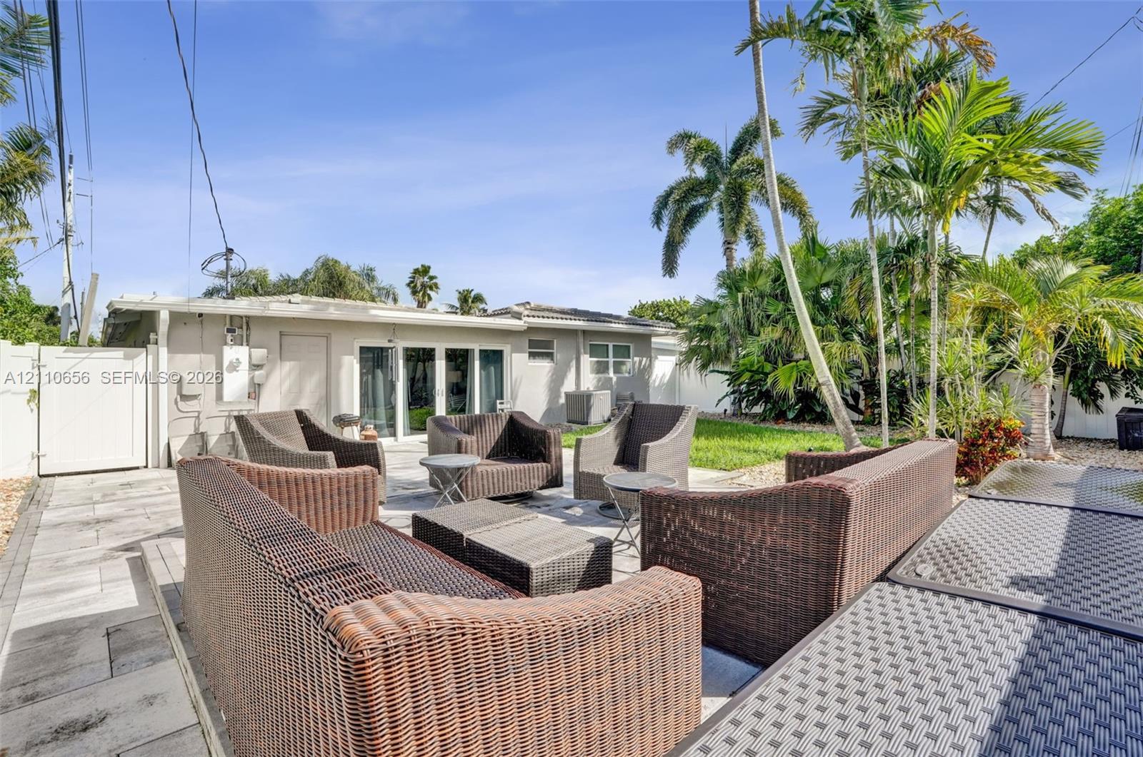 Expansive outdoor living area featuring paved patio flooring, a white privacy fence, and mature palm trees