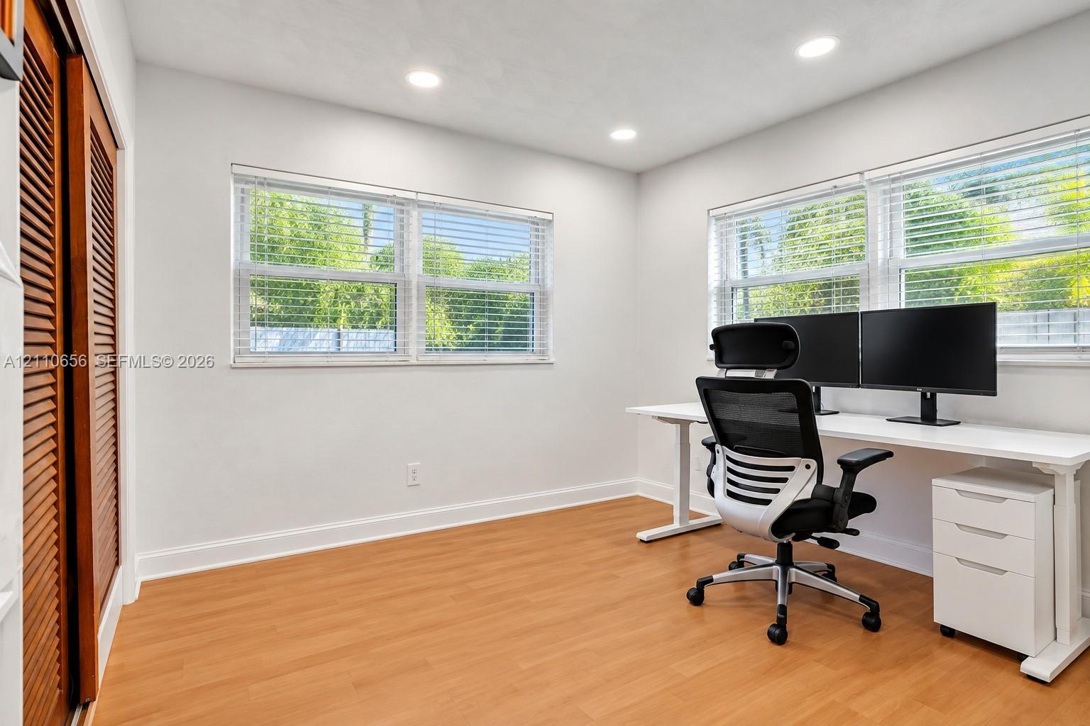 Room featuring wood-finish flooring, recessed lighting, dual windows with horizontal blinds, and a closet with louvered doors