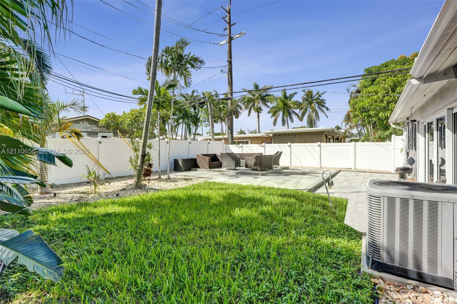 Backyard featuring a paved patio area, manicured lawn, stone landscape accents, and a perimeter vinyl privacy fence