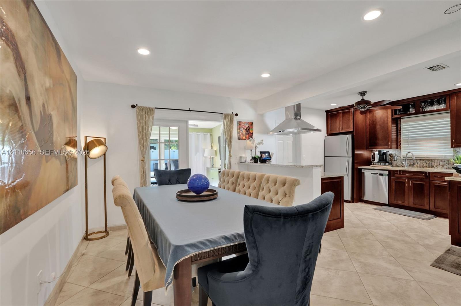 Kitchen featuring dark wood cabinetry, stainless steel appliances, a stainless steel range hood, stone-finish countertops, and tile flooring