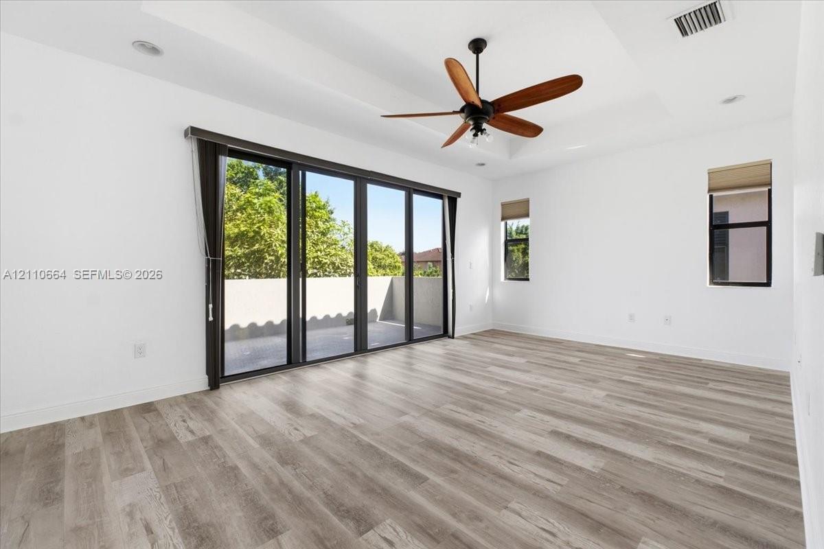 An elegant tray ceiling adds architectural distinction, while expansive multi-panel glass doors fill the space with natural light, providing access to a private balcony