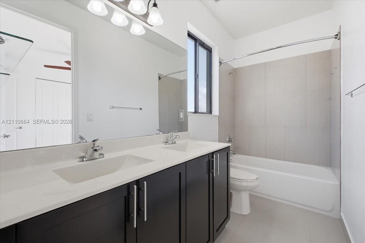 Jack-and-Jill bathroom featuring a dual-sink vanity, dark cabinetry, full-width mirror and tiled bathtub.