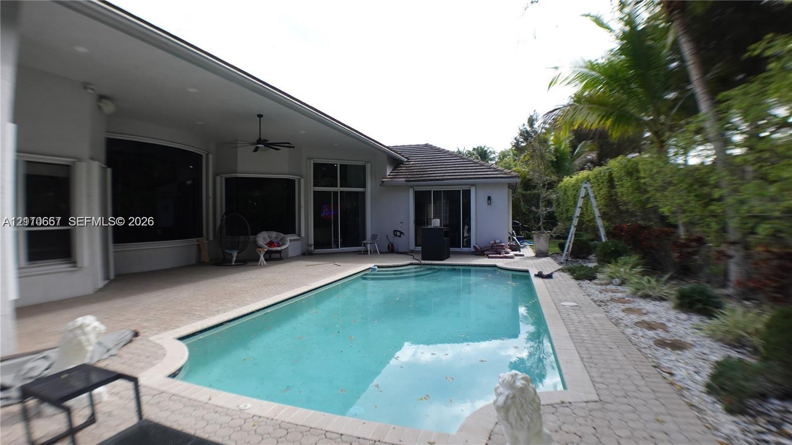 Rear exterior featuring an in-ground swimming pool, concrete paver patio, covered porch with a ceiling fan, and stucco siding