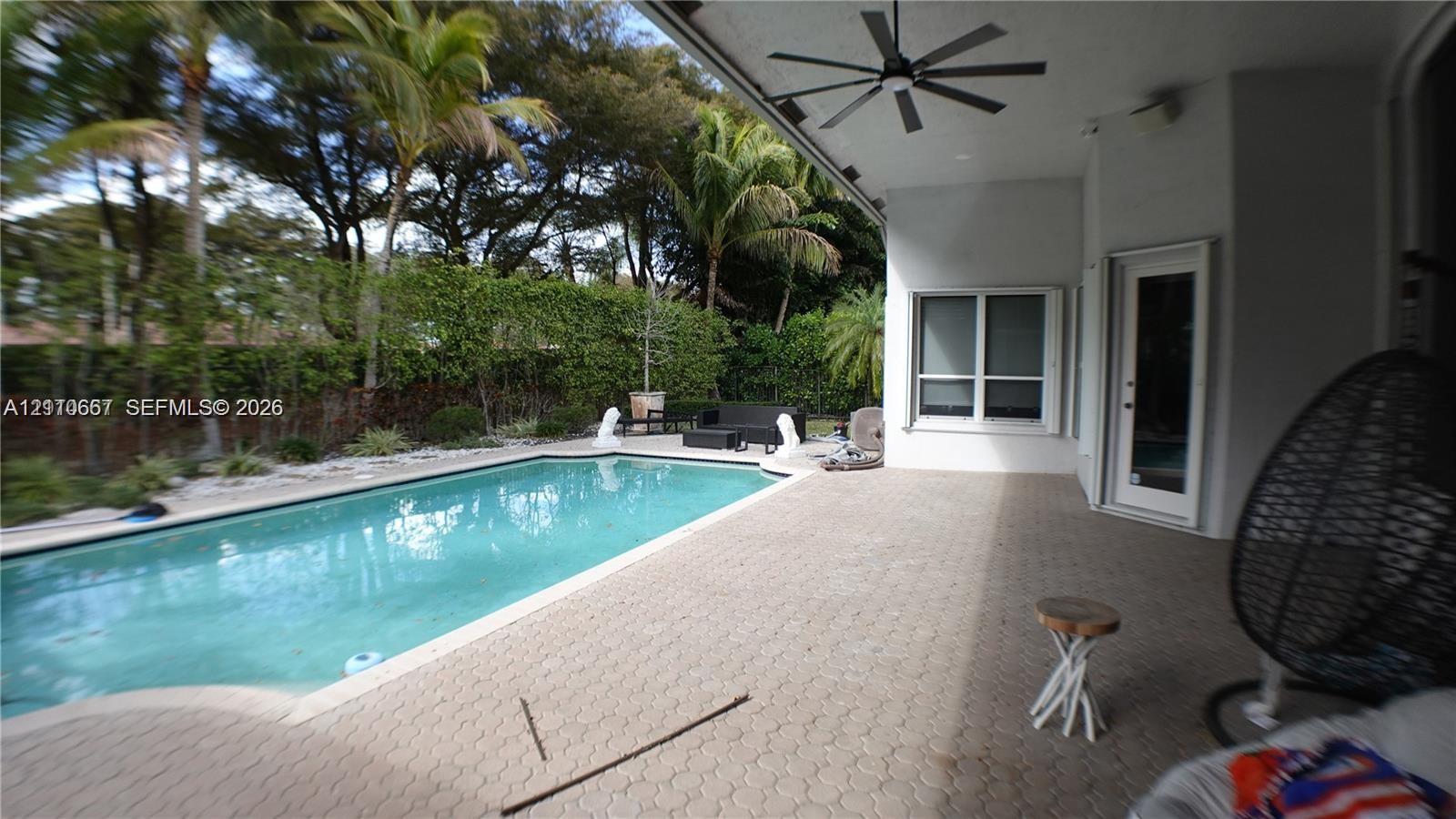 In-ground swimming pool featuring a paver patio, covered terrace, exterior lighting fixtures, and landscaped perimeter