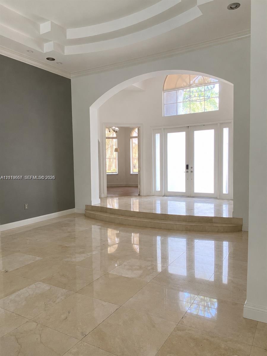 Interior space featuring multi-tiered tray ceiling, large-format polished stone flooring, expansive floor-to-ceiling windows, recessed lighting, and arched architectural detailing