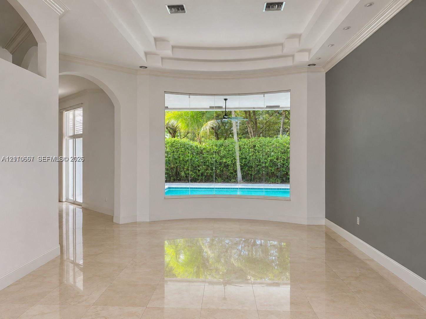 Interior space featuring polished stone flooring, recessed tray ceiling with architectural molding, and an arched entry