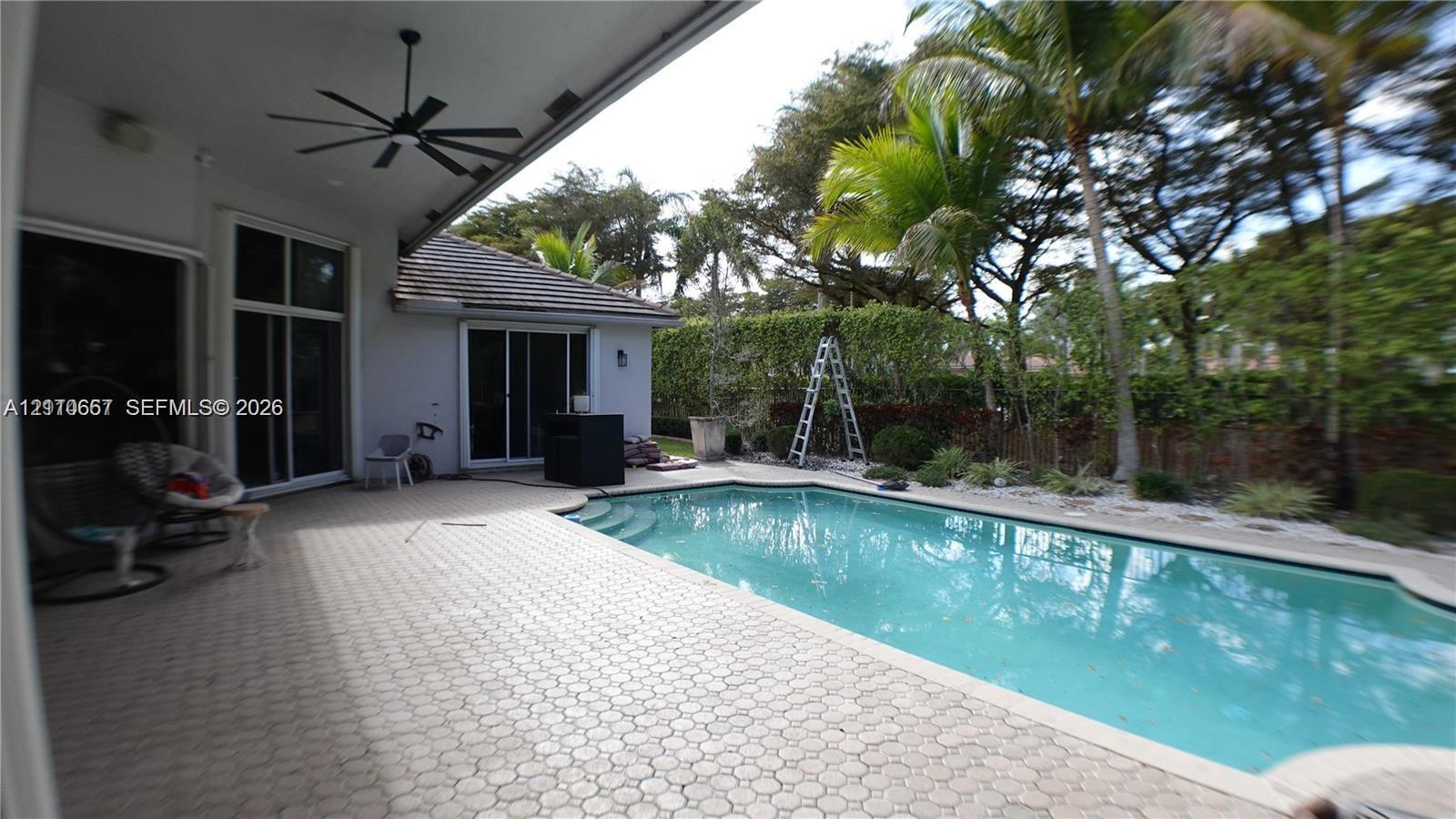 Rear patio featuring concrete paver decking, swimming pool with integrated stairs, and exterior wall-mounted lighting