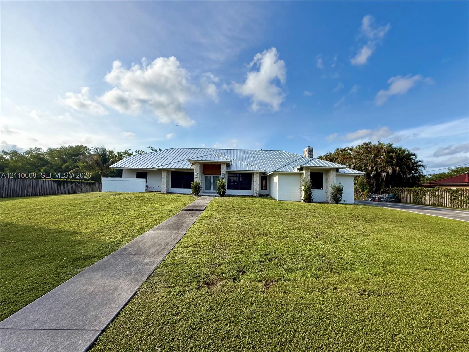 Single-story residence featuring a metal roof, stone-accented facade, expansive front lawn, and a concrete walkway