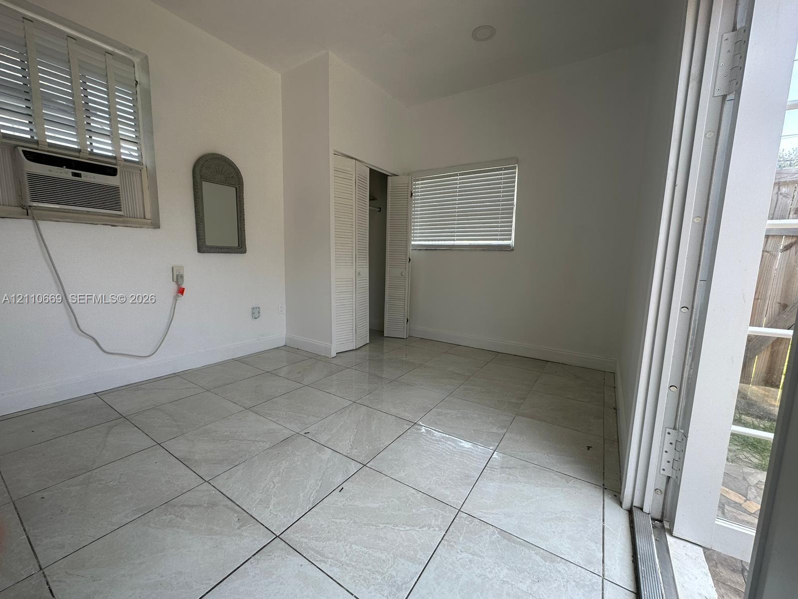 Neutral-toned tile flooring, louvered closet doors, and windows equipped with adjustable horizontal blinds