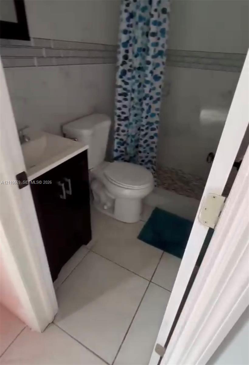 Bathroom featuring a vanity with a rectangular sink, large-format floor tile, and tiled shower surround with horizontal decorative inlay