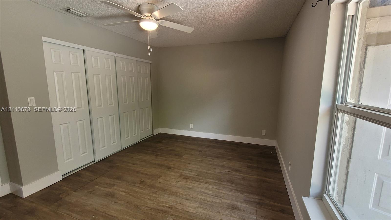 Wood-finish flooring, multi-panel sliding closet doors, ceiling fan with integrated light fixture, and large window with natural lighting Wood-finish flooring, multi-panel sliding closet doors, ceiling fan with integrated light fixture, and large window with natural lighting