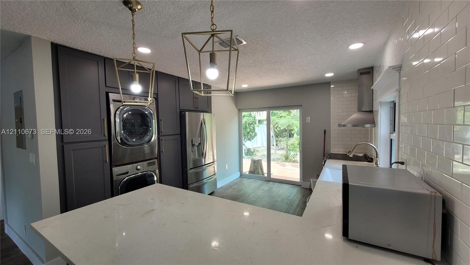 Kitchen featuring quartz countertops, white subway tile backsplash, dark-toned cabinetry, stainless steel appliances, and geometric pendant lighting Kitchen featuring quartz countertops, white subway tile backsplash, dark-toned cabinetry, stainless steel appliances, and geometric pendant lighting
