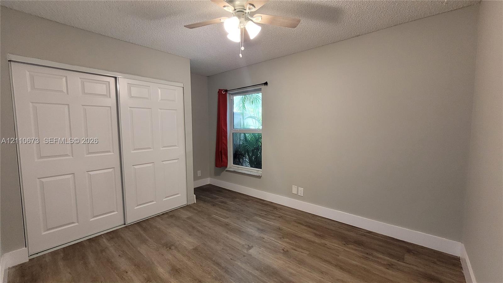Wood-finish flooring, dual-panel sliding closet doors, ceiling fan with integrated lighting, and neutral-toned wall paint