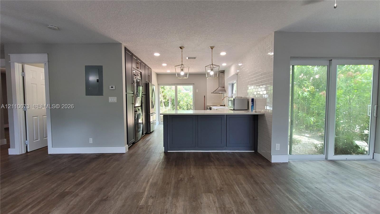 Kitchen featuring a central island with cabinetry, subway tile backsplash, stainless steel range hood, and wood-finish flooring Kitchen featuring a central island with cabinetry, subway tile backsplash, stainless steel range hood, and wood-finish flooring