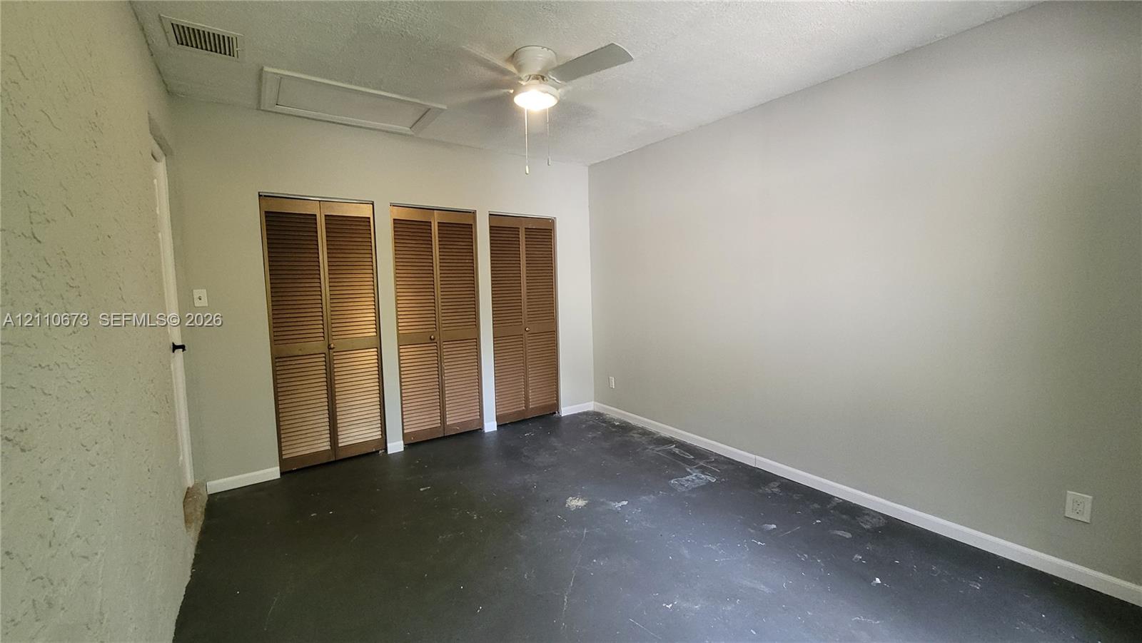 Interior space featuring three bi-fold louvered closet doors, a white ceiling fan with integrated lighting, and textured wall finish