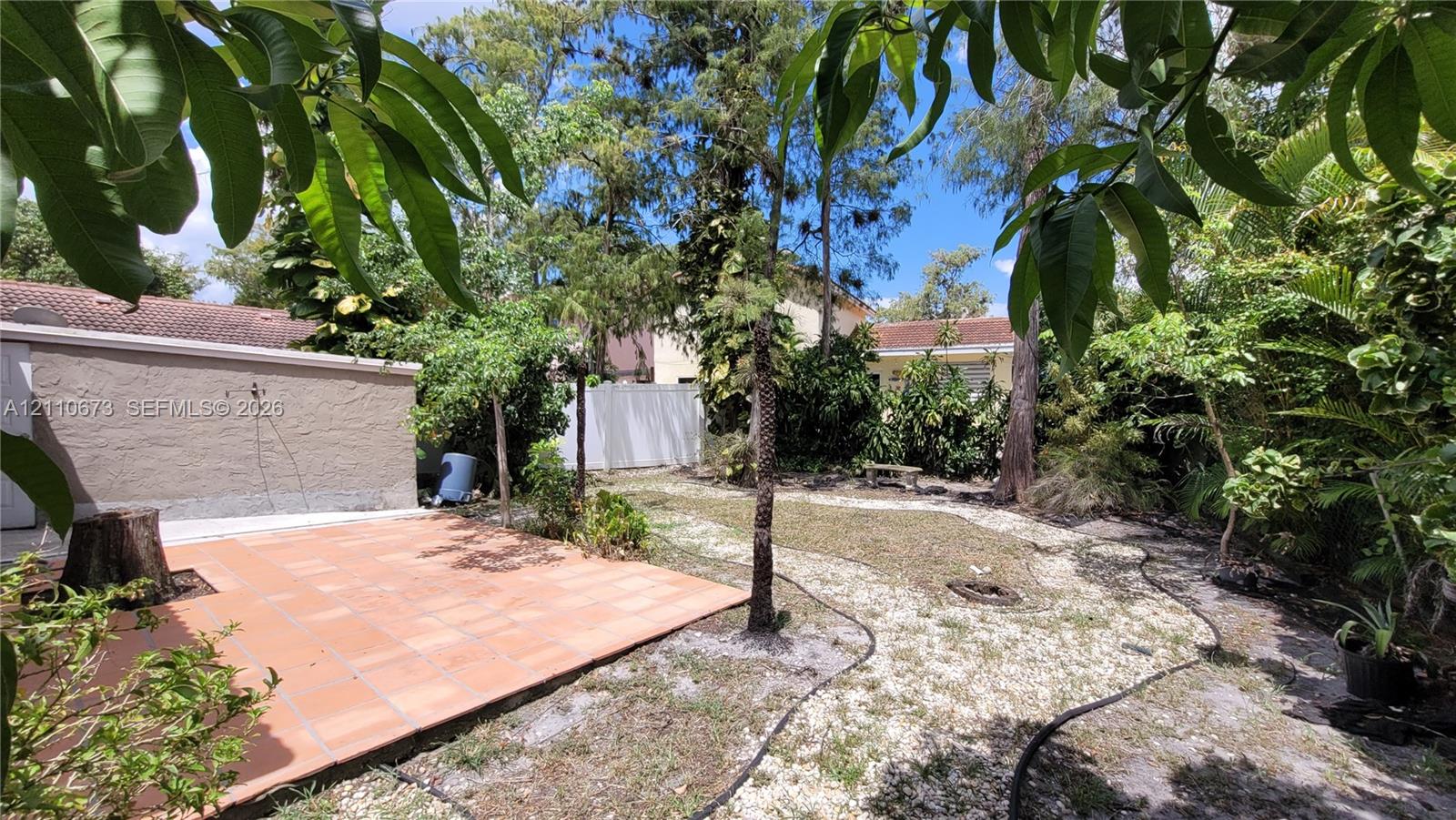 Backyard featuring a paved tile patio, light-colored gravel ground cover, privacy fencing, and mature trees