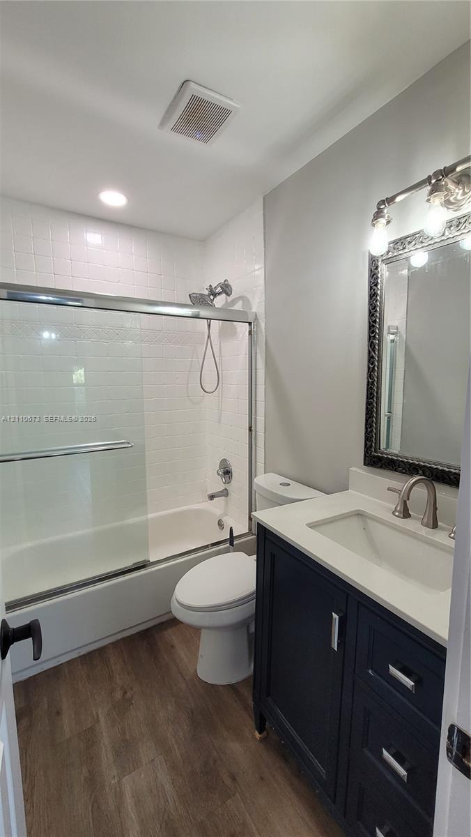 Dark-finish vanity with a light-tone countertop, tub-shower combination with sliding glass doors, white tiled shower surround, and wood-finish flooring