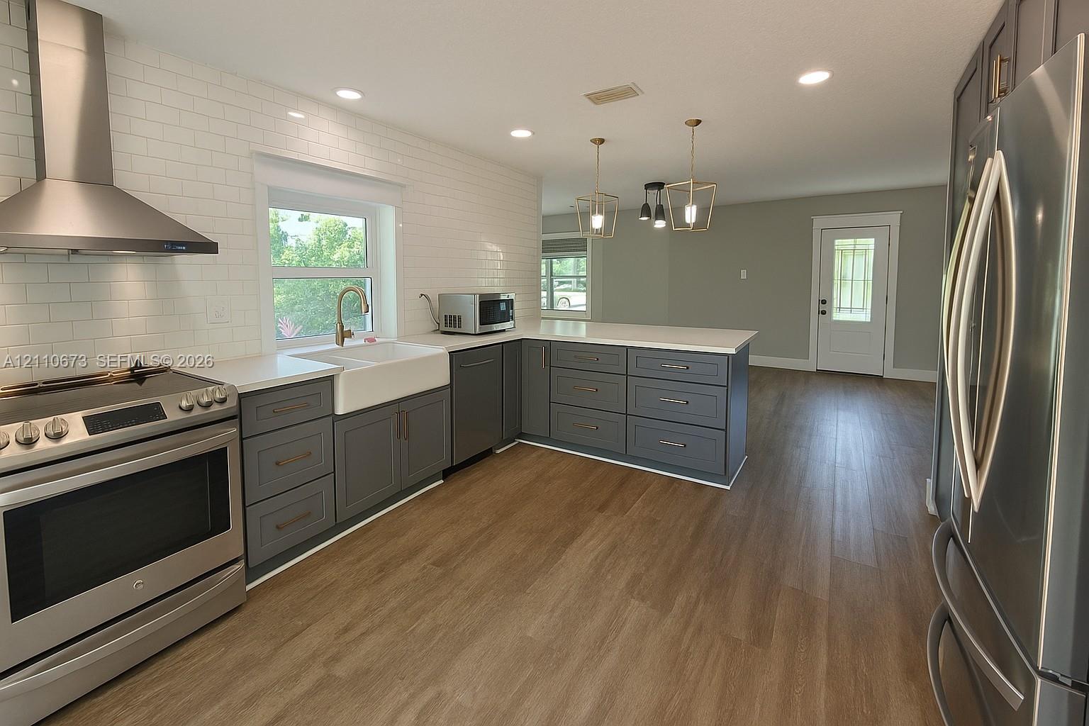 Kitchen featuring gray cabinetry, stainless steel appliances, white subway tile backsplash, white countertops, and wood-finish flooring Kitchen featuring gray cabinetry, stainless steel appliances, white subway tile backsplash, white countertops, and wood-finish flooring