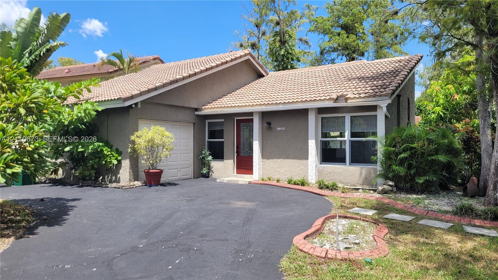 Stucco exterior with a tiled roof, asphalt driveway, attached one-car garage, and red-trimmed front entry