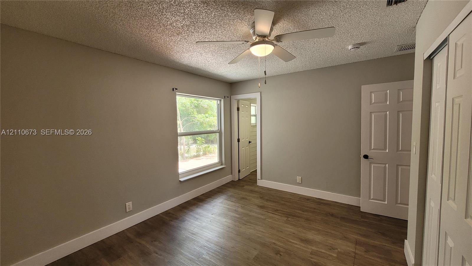 Room featuring wood-finish flooring, a ceiling fan with integrated lighting, a single-pane window, and white paneled doors Room featuring wood-finish flooring, a ceiling fan with integrated lighting, a single-pane window, and white paneled doors