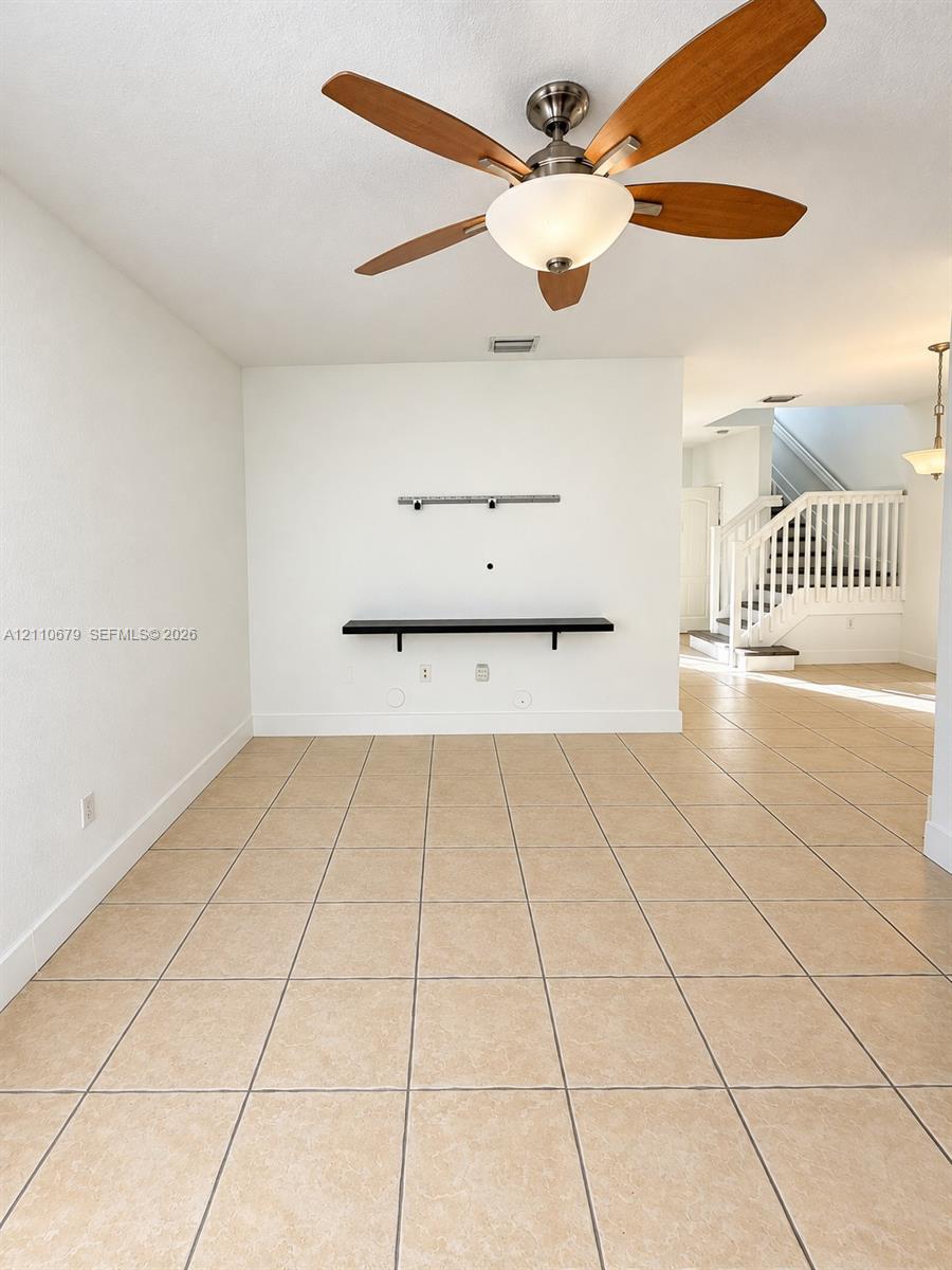 Ceramic tile flooring, ceiling fan with integrated lighting, wall-mounted display shelving, and a painted wooden staircase with white balusters