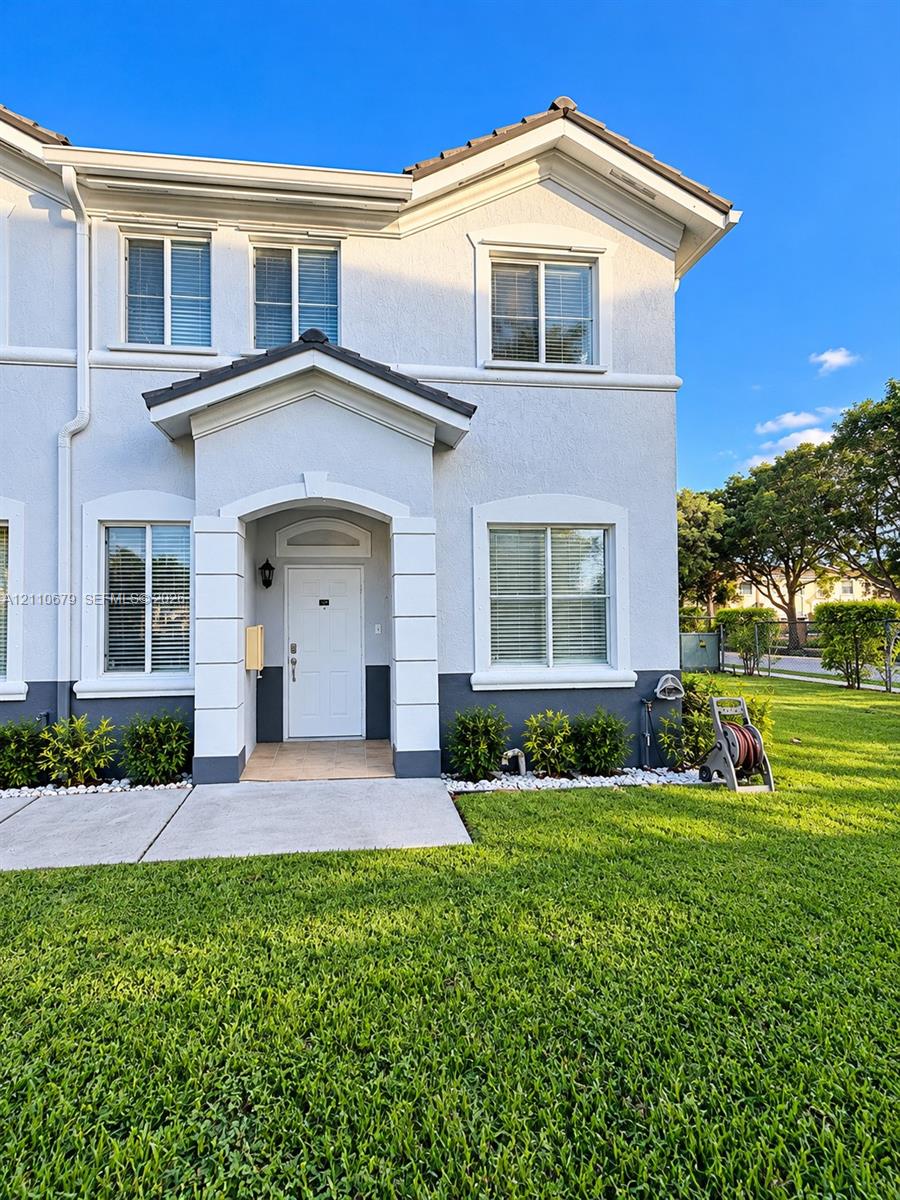 Two-story exterior featuring light-toned stucco, an arched covered entryway with decorative pillar detailing, dual-tone facade, concrete walkway, and shingled roof