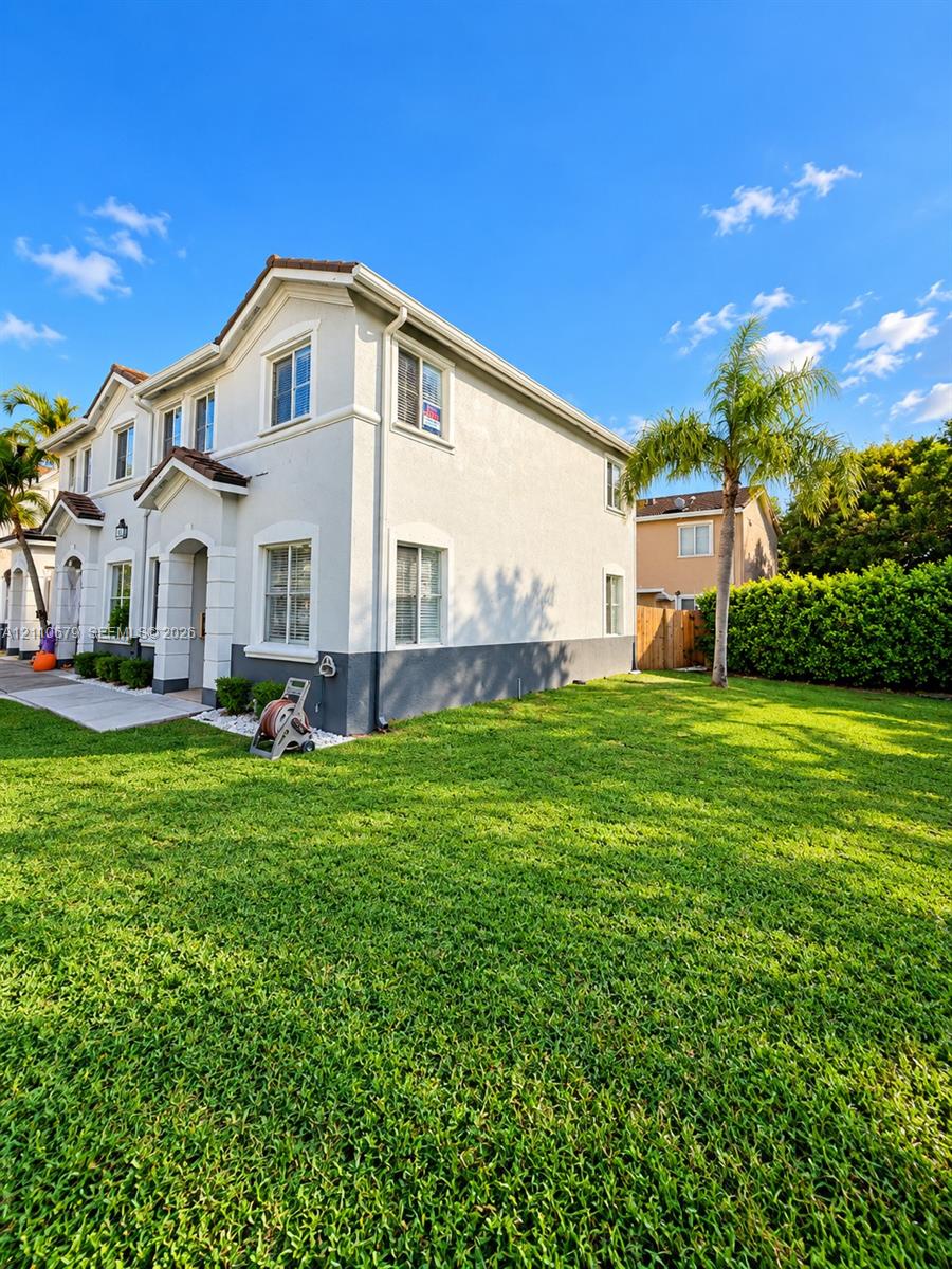 Two-story exterior featuring a light-toned stucco facade with dual-tone trim, a concrete walkway, and an expansive lawn