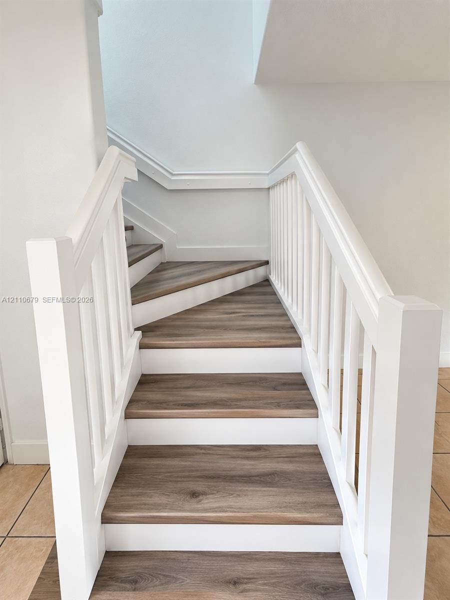 Staircase featuring wood-finish treads, white risers, square white balusters, and a solid post railing