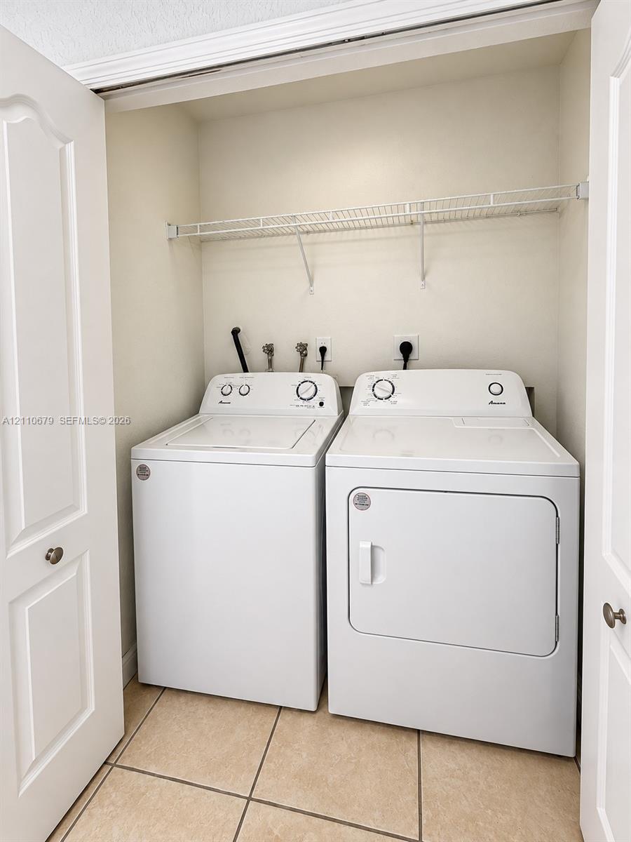Laundry closet featuring tile flooring, white bi-fold doors, and a wall-mounted wire storage shelf