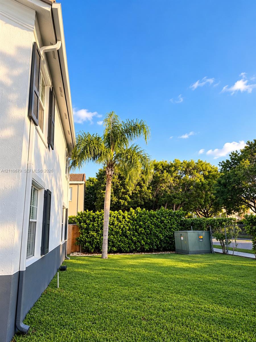 Exterior side yard featuring stucco siding, two-tone paint, dark shutters, manicured lawn, and mature landscaping