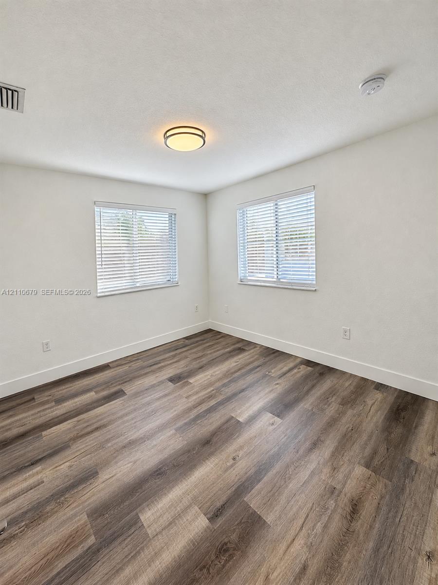 Room featuring wood-finish flooring, dual windows with blinds, and a central flush-mount light fixture