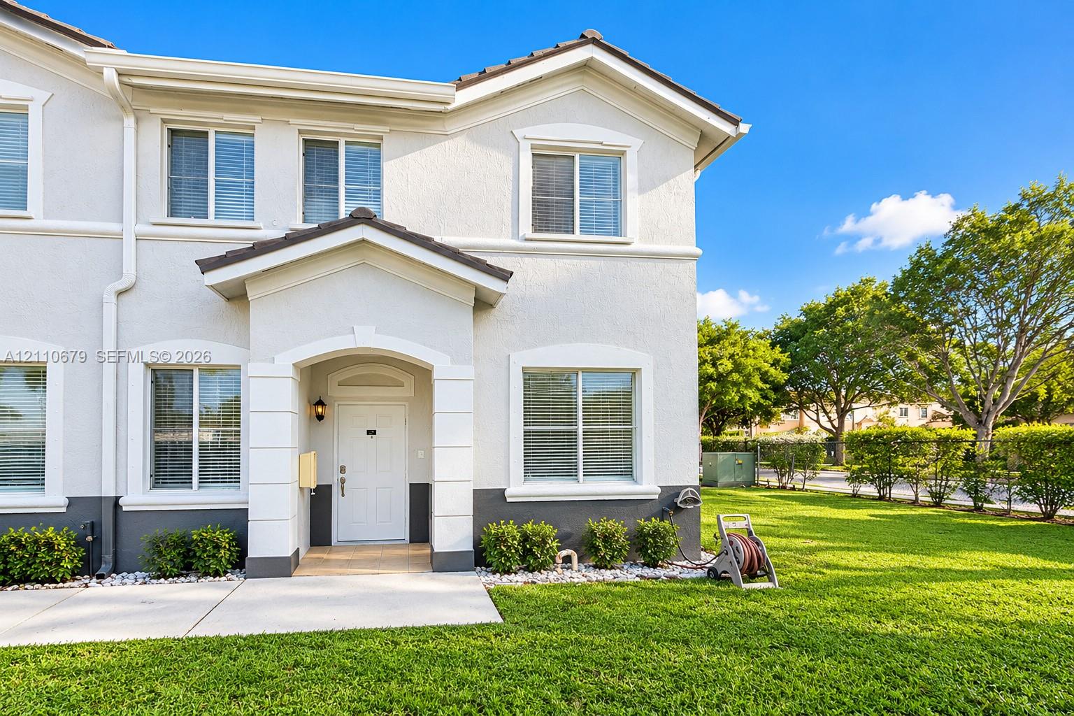 Stucco exterior featuring dual-tone paint, a covered entryway with stone-finish trim, multiple grid-pattern windows, and a paved walkway Stucco exterior featuring dual-tone paint, a covered entryway with stone-finish trim, multiple grid-pattern windows, and a paved walkway