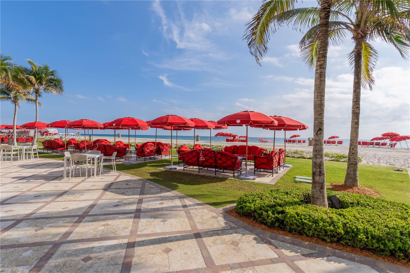 Outdoor terrace featuring stone-tiled flooring with masonry grid pattern, mature palm trees, manicured lawn, and direct oceanfront access