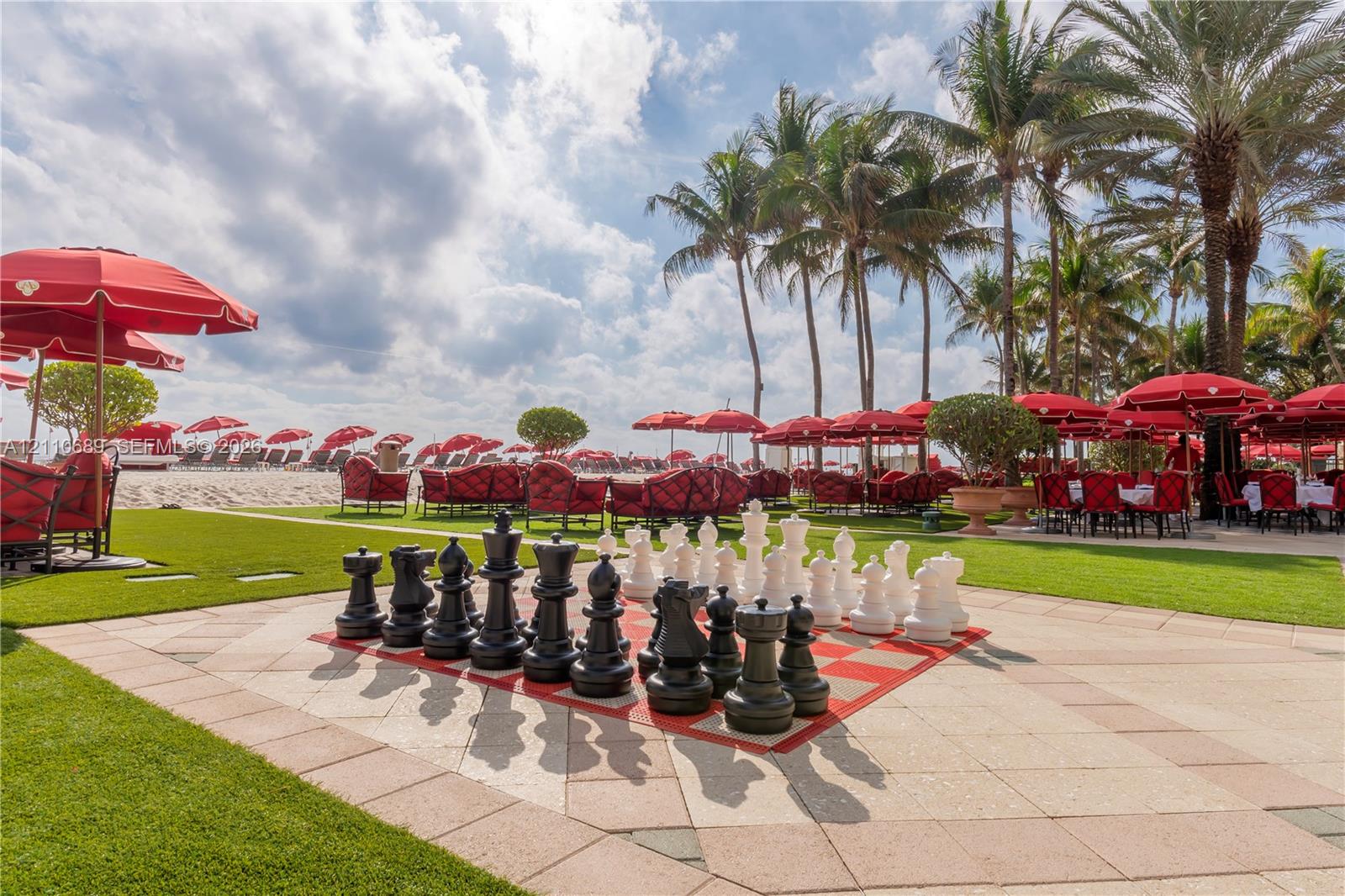 Outdoor terrace featuring a large-scale built-in chessboard, manicured lawn, and mature palm trees