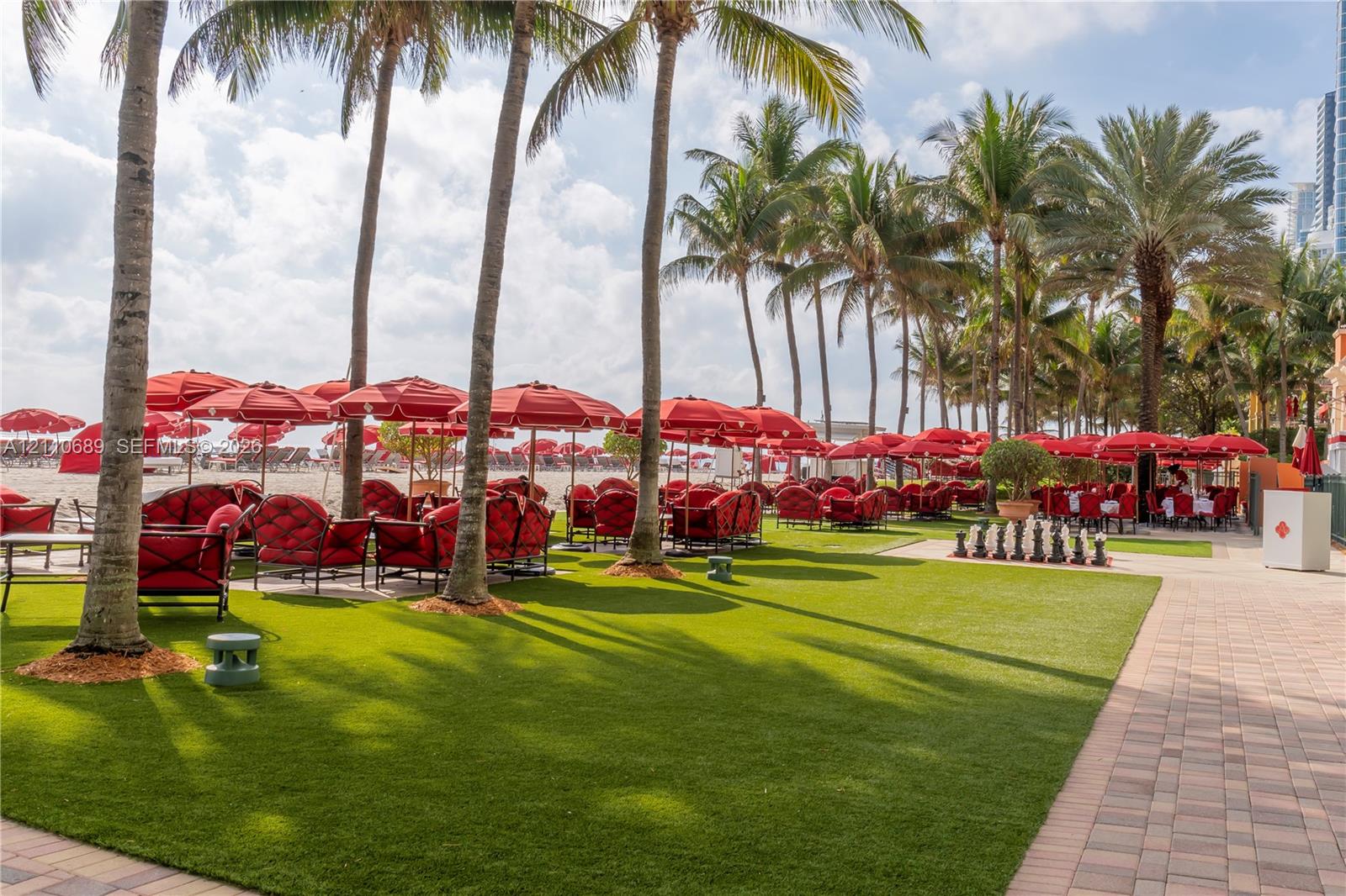 Outdoor space featuring a manicured lawn, mature palm trees, interlocking paver walkway, and permanent exterior hardscaping