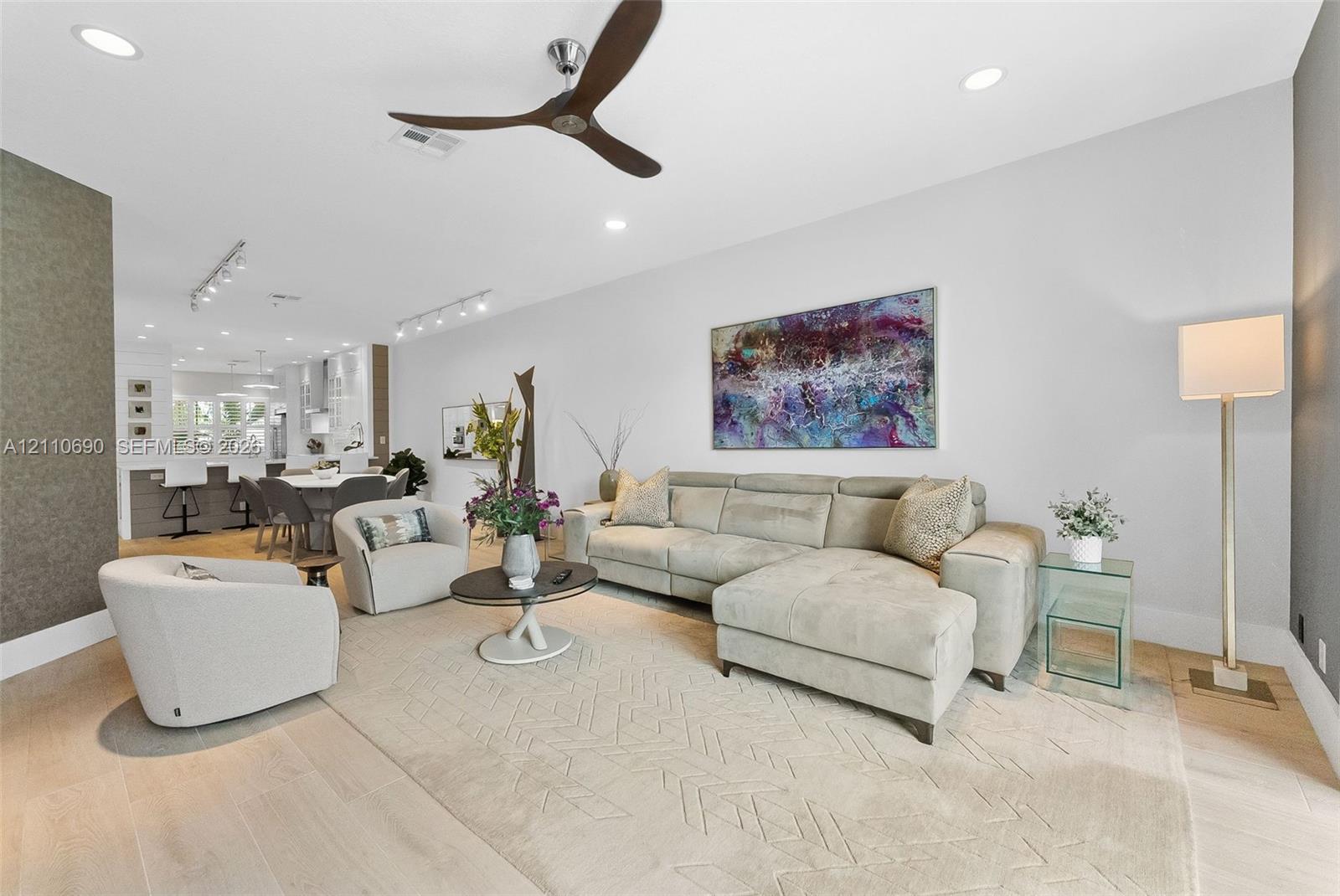 Open-concept interior featuring light-toned wood-finish flooring, recessed lighting, track lighting, and a contemporary three-blade ceiling fan Open-concept interior featuring light-toned wood-finish flooring, recessed lighting, track lighting, and a contemporary three-blade ceiling fan