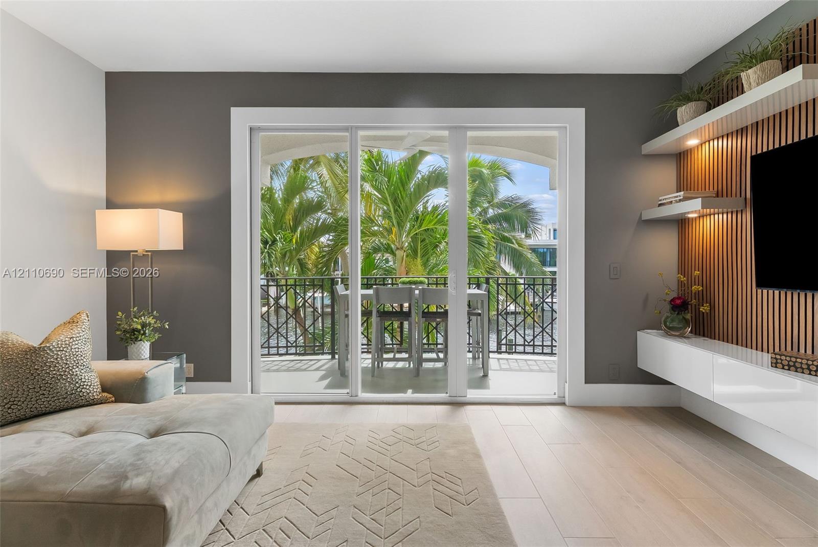 Sliding glass doors opening to a covered balcony with decorative metal railing, wood-slat accent wall with integrated shelving, and white high-gloss floating cabinetry Sliding glass doors opening to a covered balcony with decorative metal railing, wood-slat accent wall with integrated shelving, and white high-gloss floating cabinetry
