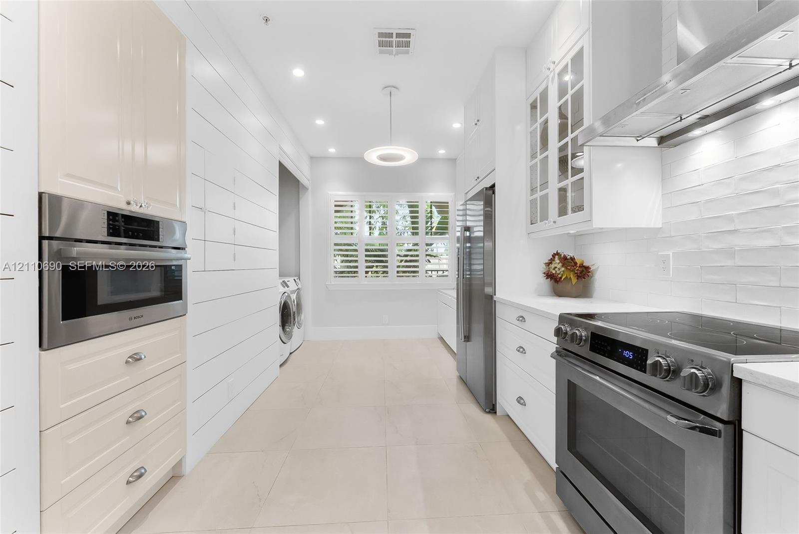 Kitchen featuring white Shaker-style cabinetry, stainless steel appliances, shiplap wall paneling, tile flooring, and interior window shutters
