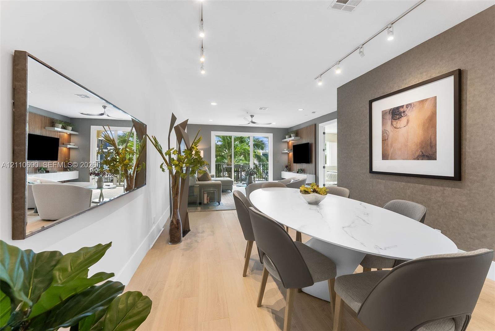 Dining area featuring wood-finish flooring, a wall-mounted oversized mirror, textured accent wall, and adjustable track lighting Dining area featuring wood-finish flooring, a wall-mounted oversized mirror, textured accent wall, and adjustable track lighting