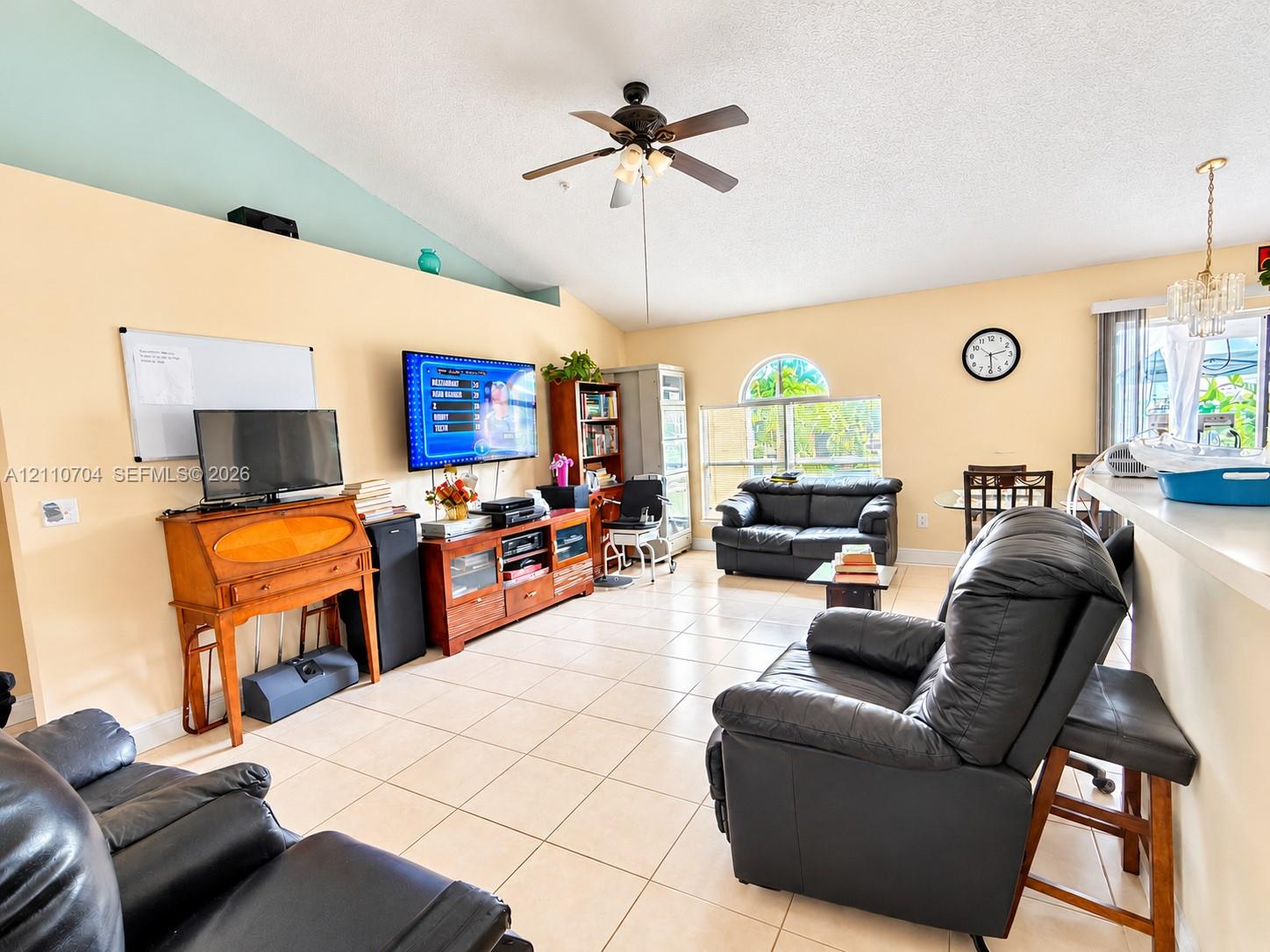 Vaulted ceilings featuring a central overhead fan, ceramic tile flooring, arched window, and a breakfast bar