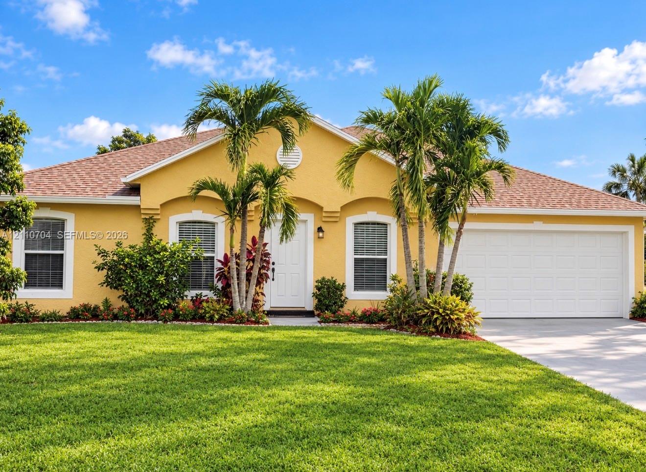 Single-story exterior featuring a stucco facade, an attached two-car garage, arched window trim, and a manicured lawn with mature palm landscaping